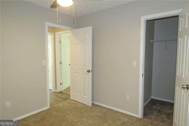 unfurnished bedroom with a closet, dark colored carpet, ceiling fan, and a walk in closet