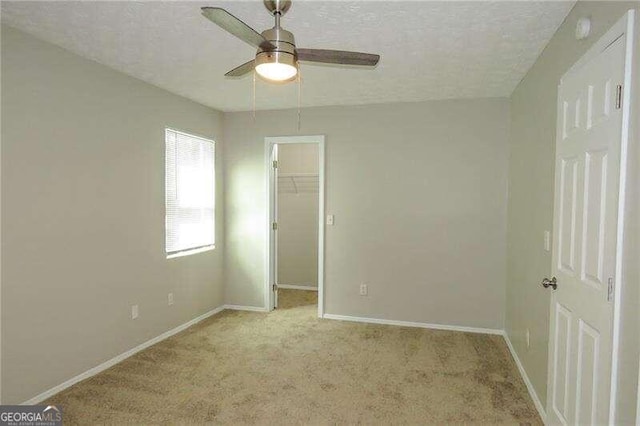 unfurnished bedroom with a closet, ceiling fan, a textured ceiling, light colored carpet, and a walk in closet