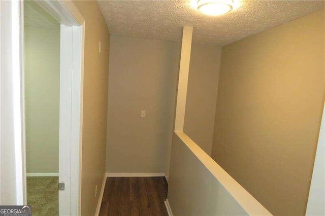 hall with dark carpet and a textured ceiling