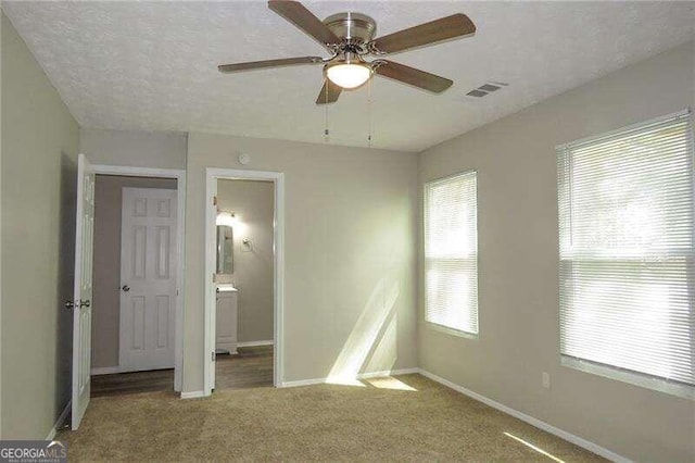 unfurnished bedroom with ceiling fan, dark carpet, ensuite bathroom, and a textured ceiling