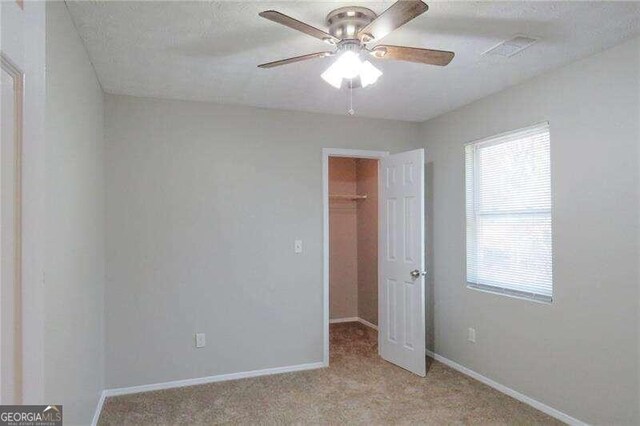 empty room with light colored carpet, ceiling fan, and a healthy amount of sunlight