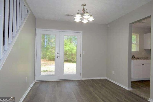 doorway to outside with a healthy amount of sunlight, dark wood-type flooring, and an inviting chandelier