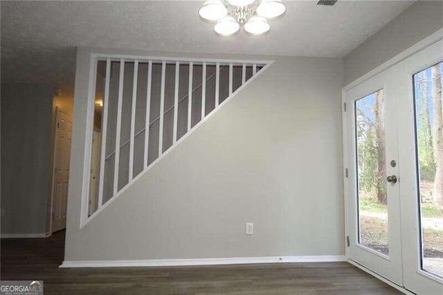 spare room featuring a healthy amount of sunlight, a textured ceiling, dark hardwood / wood-style flooring, and a notable chandelier