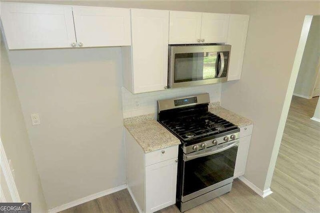 kitchen featuring light hardwood / wood-style floors, tasteful backsplash, white cabinetry, stainless steel appliances, and light stone countertops