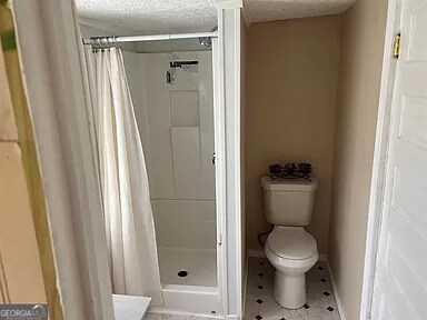 bathroom featuring tile flooring, a shower with shower curtain, toilet, and a textured ceiling