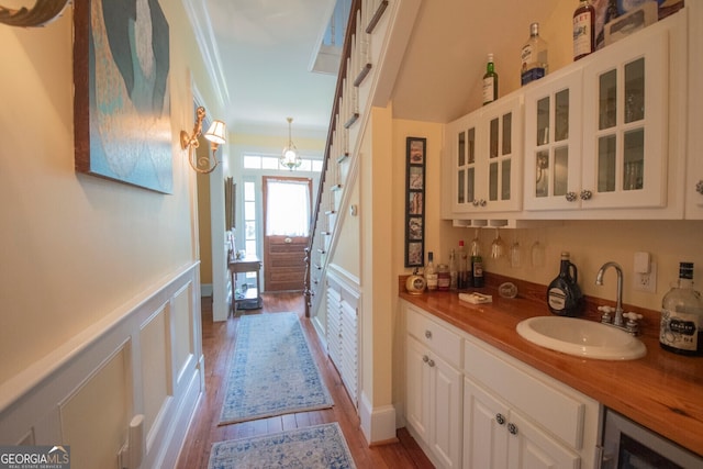 bar featuring white cabinets, beverage cooler, ornamental molding, light hardwood / wood-style floors, and sink