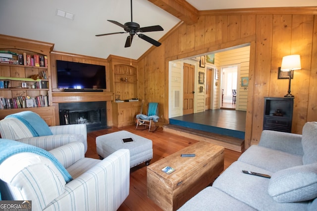 living room featuring wood walls, vaulted ceiling with beams, hardwood / wood-style floors, ceiling fan, and built in shelves