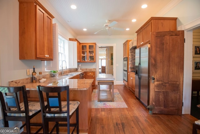 kitchen with hardwood / wood-style flooring, a kitchen breakfast bar, kitchen peninsula, sink, and appliances with stainless steel finishes