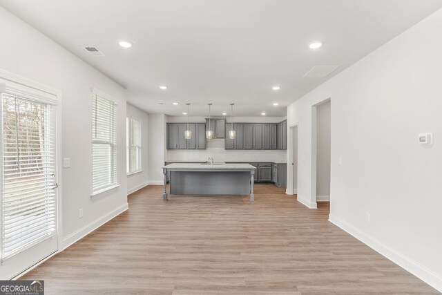 kitchen featuring gray cabinetry, sink, hanging light fixtures, light wood-type flooring, and an island with sink