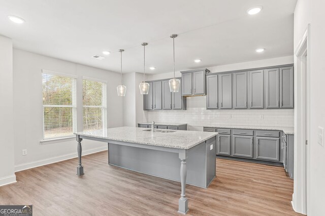 kitchen with light wood-type flooring, a center island with sink, gray cabinetry, and sink