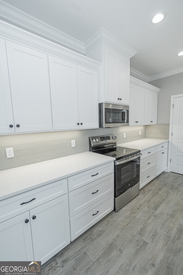 kitchen featuring appliances with stainless steel finishes, crown molding, tasteful backsplash, white cabinets, and light wood-type flooring