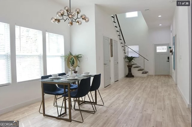 dining room featuring a chandelier, a wealth of natural light, a towering ceiling, and light hardwood / wood-style floors