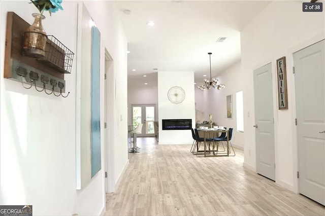 hallway with a high ceiling, an inviting chandelier, and light hardwood / wood-style flooring