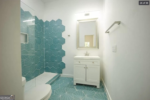 bathroom featuring tile patterned floors, vanity, a tile shower, and toilet