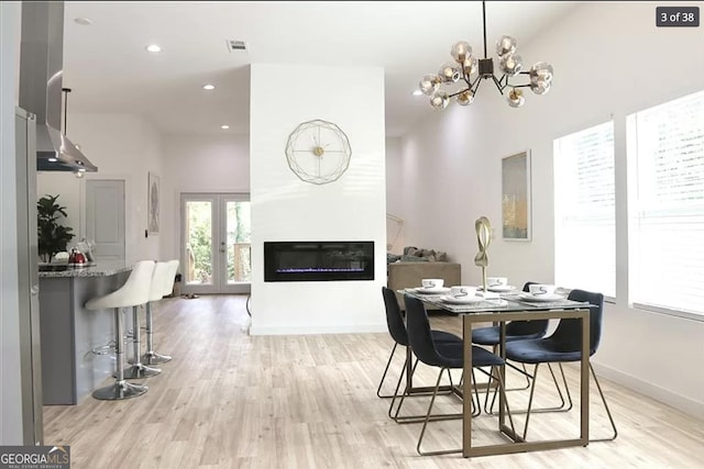 dining space featuring a fireplace, a high ceiling, light hardwood / wood-style floors, and an inviting chandelier