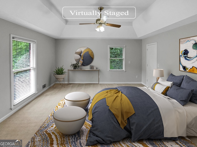 bedroom with multiple windows, light carpet, ceiling fan, and a tray ceiling