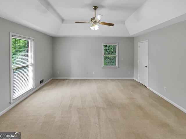 spare room featuring light colored carpet, ceiling fan, a tray ceiling, and plenty of natural light