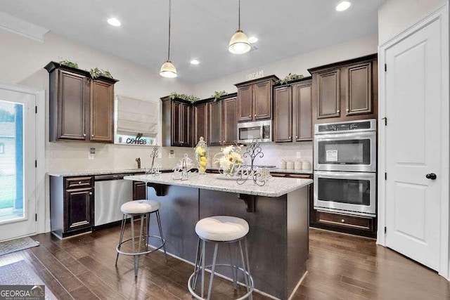 kitchen with pendant lighting, stainless steel appliances, dark wood-type flooring, and light stone counters