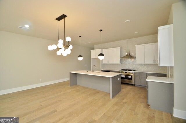 kitchen featuring sink, high end stainless steel range oven, hanging light fixtures, tasteful backsplash, and white cabinetry