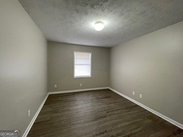 spare room featuring dark wood-style floors, a textured ceiling, and baseboards