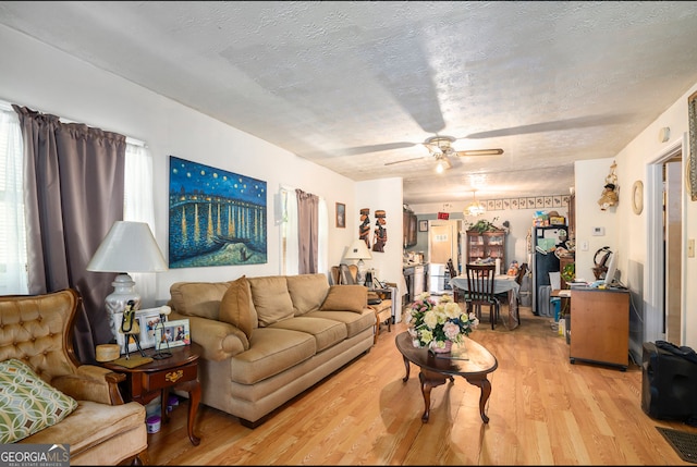 living room featuring ceiling fan, light hardwood / wood-style flooring, and a textured ceiling