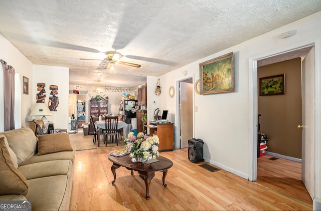 living room with ceiling fan, light wood-type flooring, and a textured ceiling