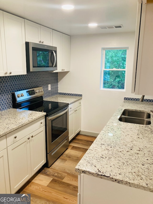 kitchen with tasteful backsplash, appliances with stainless steel finishes, sink, and light stone countertops