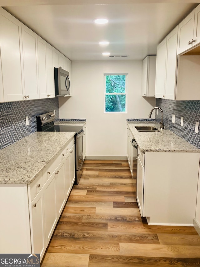 kitchen featuring appliances with stainless steel finishes, backsplash, light hardwood / wood-style floors, white cabinetry, and sink