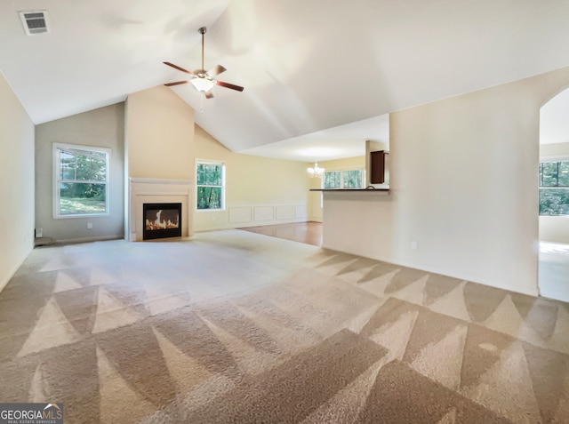 unfurnished living room with a healthy amount of sunlight, vaulted ceiling, ceiling fan, and light carpet