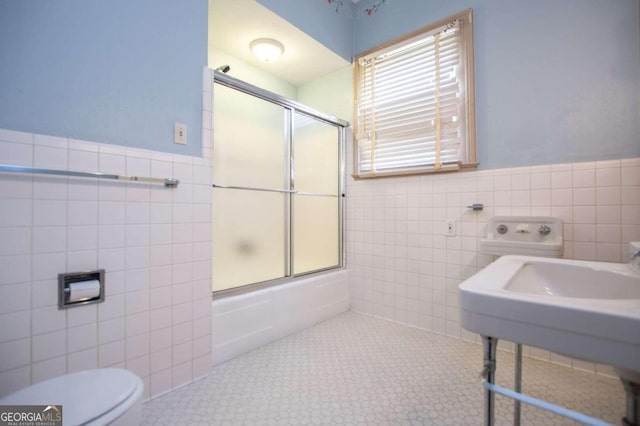 bathroom with tile patterned flooring, tile walls, bath / shower combo with glass door, and toilet