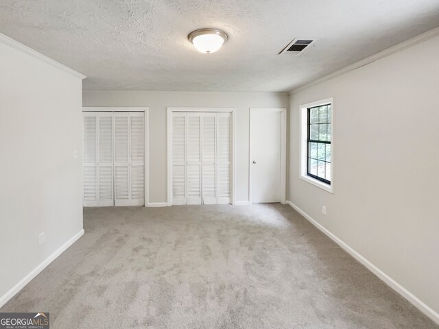 unfurnished bedroom featuring a textured ceiling, carpet, crown molding, and multiple closets