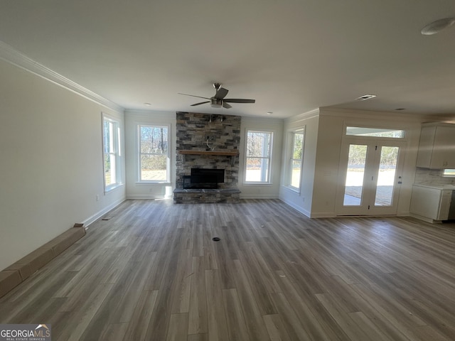 unfurnished living room with light wood-type flooring, a stone fireplace, ceiling fan, and ornamental molding