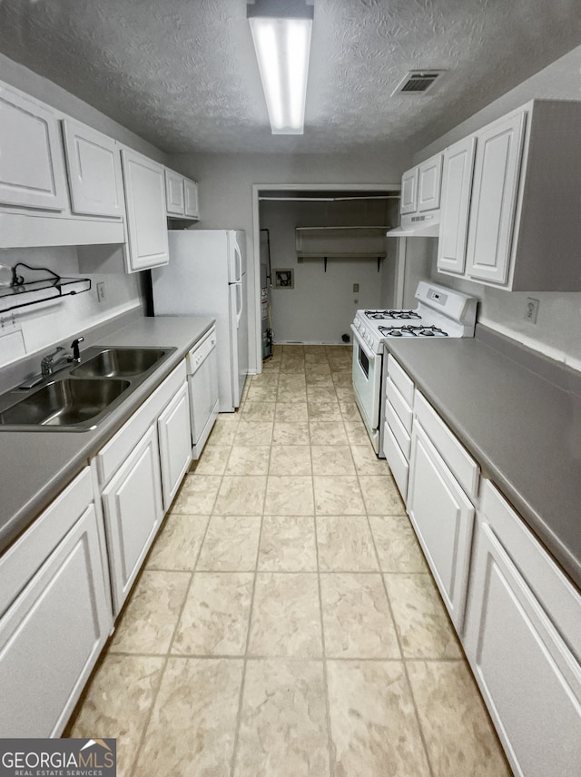 kitchen with light tile floors, a textured ceiling, sink, white appliances, and white cabinetry