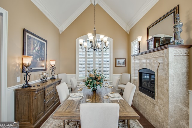 dining room featuring a notable chandelier, a tiled fireplace, lofted ceiling, crown molding, and wood-type flooring