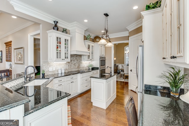 kitchen featuring light hardwood / wood-style floors, an island with sink, white cabinetry, sink, and pendant lighting