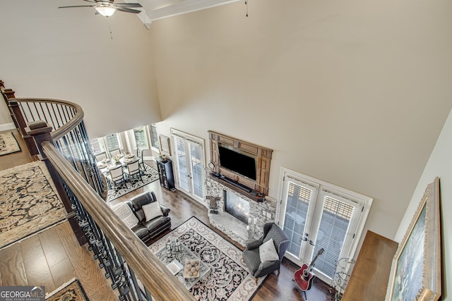 living room featuring ceiling fan, dark hardwood / wood-style flooring, a stone fireplace, and a high ceiling