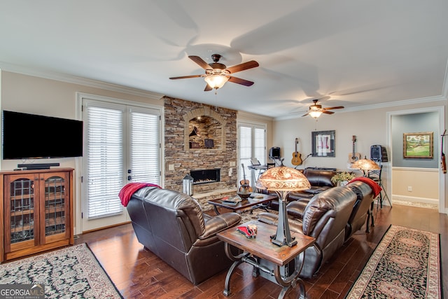 living room featuring ornamental molding, wood-type flooring, ceiling fan, and a stone fireplace