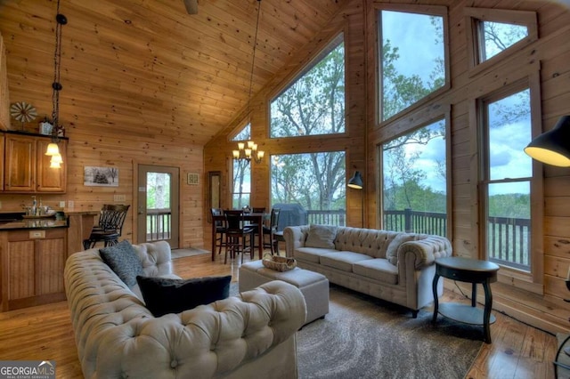 living room with high vaulted ceiling, light wood-type flooring, wooden walls, wooden ceiling, and an inviting chandelier