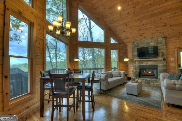 dining room featuring high vaulted ceiling, wood walls, hardwood / wood-style floors, and a stone fireplace