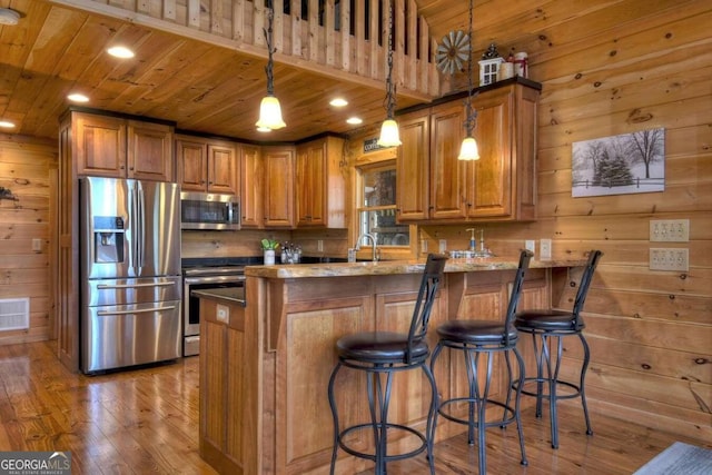 kitchen with pendant lighting, stainless steel appliances, light wood-type flooring, and wooden walls