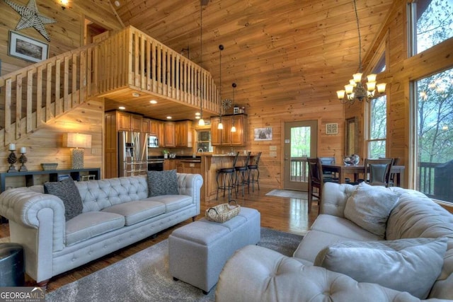 living room featuring wood-type flooring, wood walls, high vaulted ceiling, and a notable chandelier