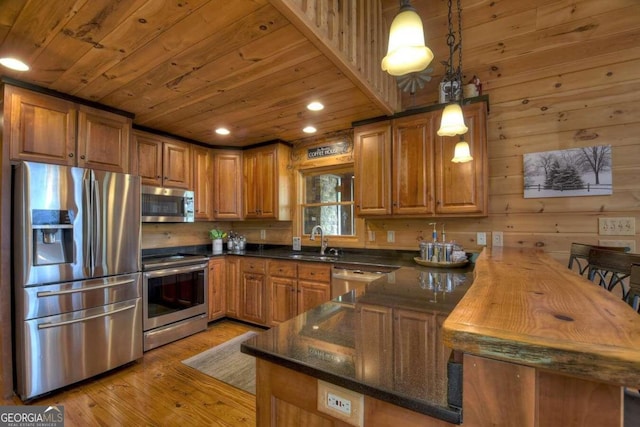 kitchen featuring sink, wood walls, hanging light fixtures, stainless steel appliances, and light hardwood / wood-style flooring