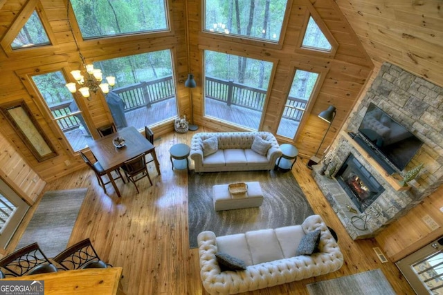 living room with high vaulted ceiling, wood-type flooring, wood walls, and a stone fireplace