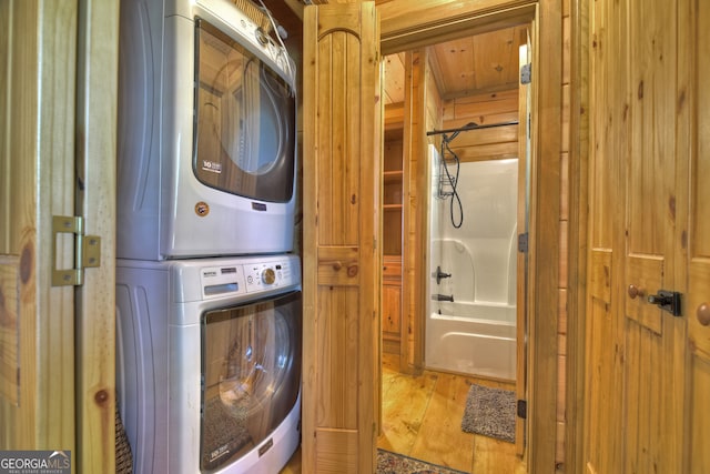 laundry room with light hardwood / wood-style flooring, stacked washer / dryer, and wood walls