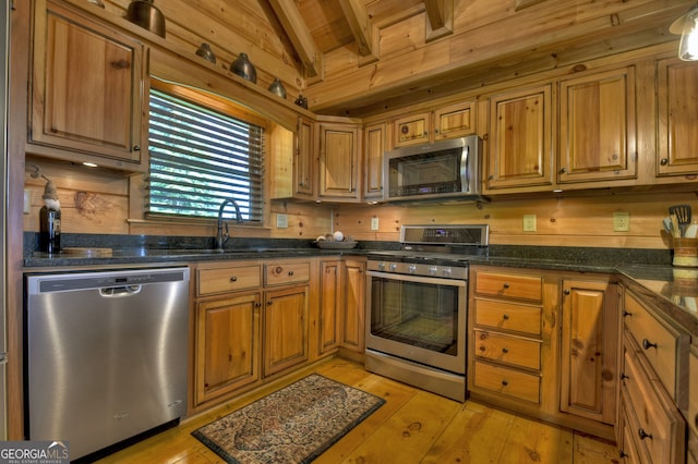 kitchen featuring wood walls, stainless steel appliances, light hardwood / wood-style floors, and vaulted ceiling with beams