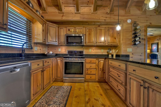 kitchen with appliances with stainless steel finishes, light wood-type flooring, beam ceiling, wood walls, and pendant lighting