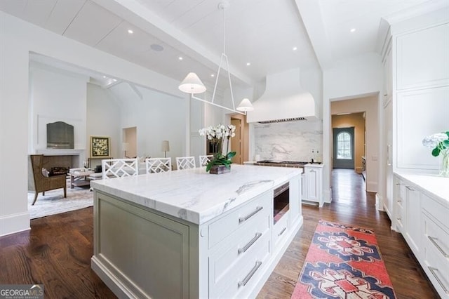 kitchen featuring a kitchen island, dark hardwood / wood-style floors, custom range hood, light stone counters, and stainless steel microwave