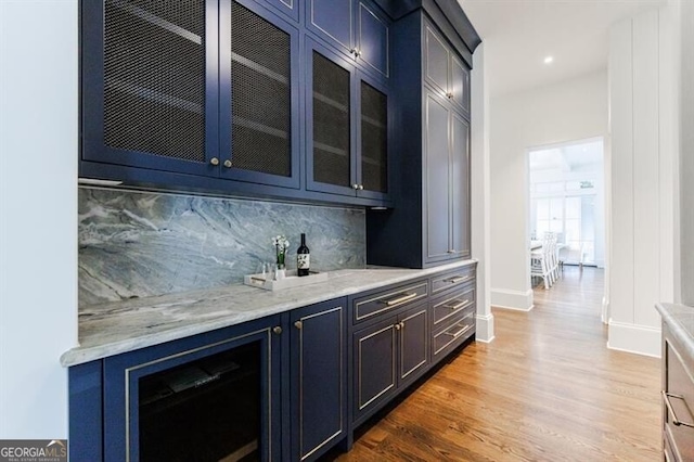 bar with tasteful backsplash, hardwood / wood-style floors, light stone counters, and blue cabinetry