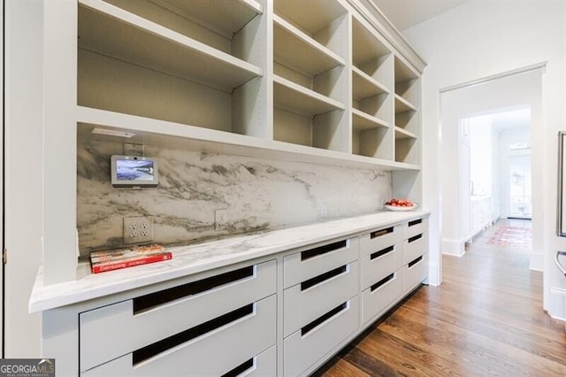 bar with tasteful backsplash, wood-type flooring, light stone counters, and white cabinets