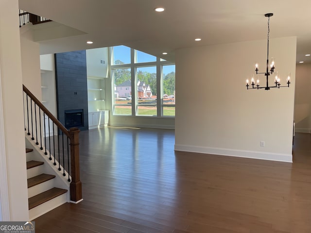 unfurnished living room featuring brick wall, an inviting chandelier, dark hardwood / wood-style floors, and a large fireplace